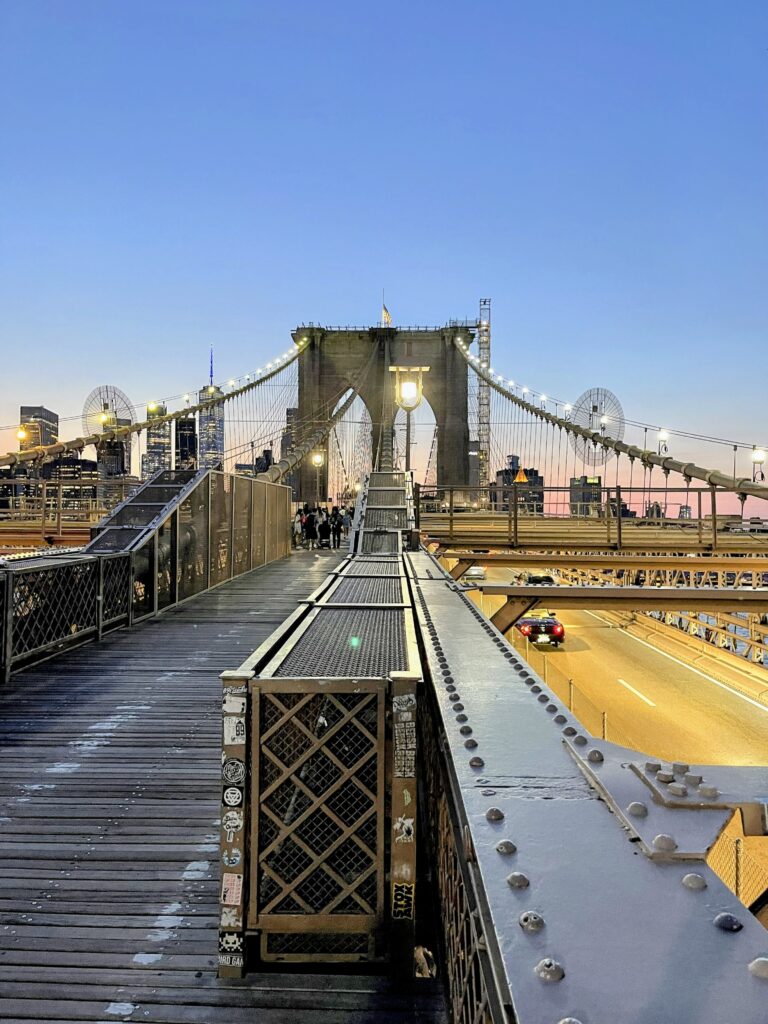Brooklyn Bridge at dusk with glowing lights and pedestrians on the walkway—an iconic and free New York City experience.