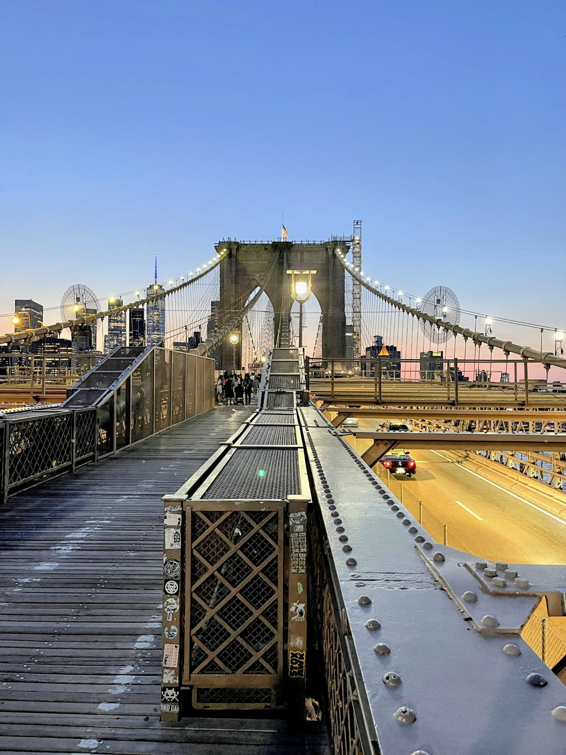 Brooklyn Bridge at dusk with glowing lights and pedestrians on the walkway—an iconic and free New York City experience.