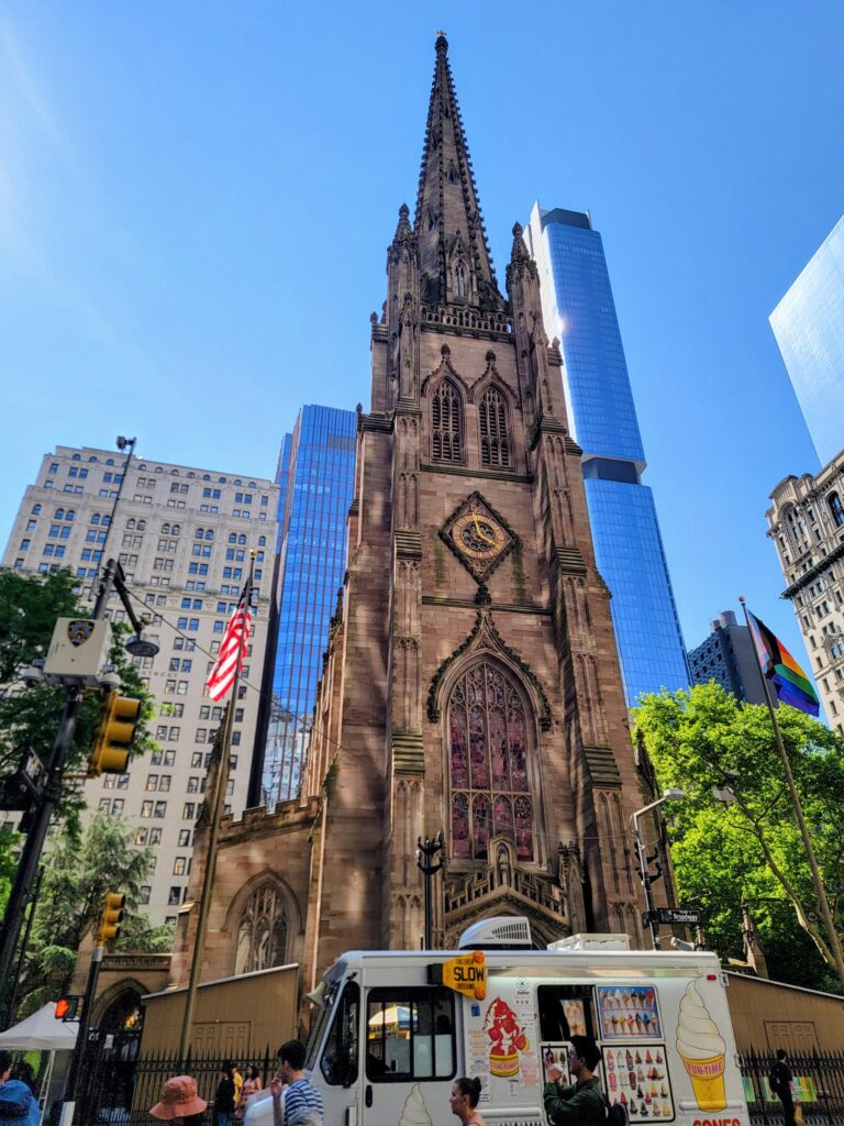 Trinity Church in NYC with Gothic architecture, surrounded by skyscrapers and a colorful ice cream truck—an urban blend of old and new, showcasing one of the hidden gems in New York.