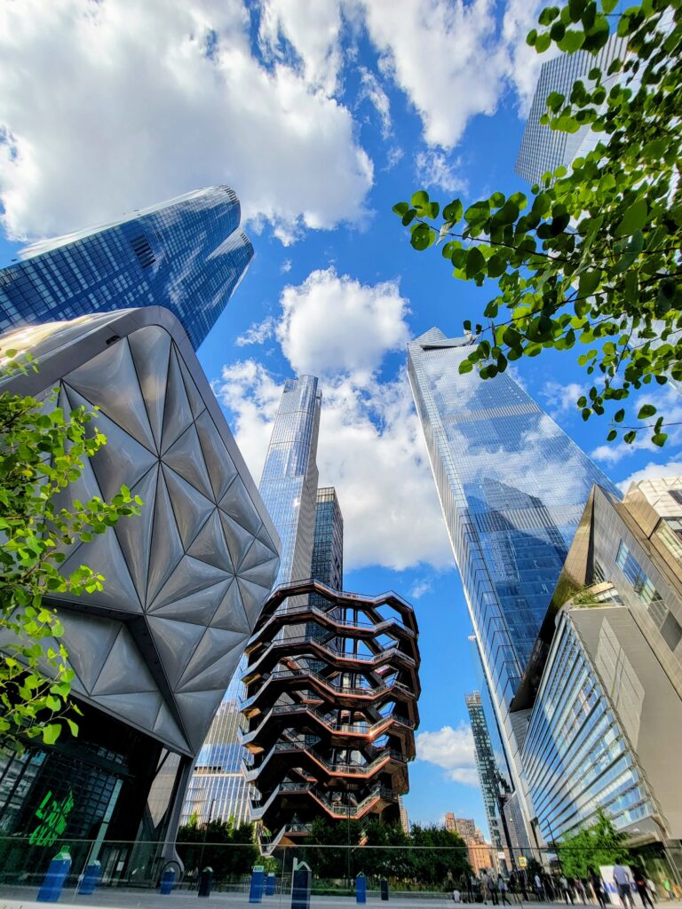 The Vessel at Hudson Yards, a honeycomb-like public art structure surrounded by glass skyscrapers and greenery, representing modern design in New York City.