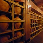 Interior view of a corridor lined with clay pots on wooden shelves, illuminated by warm lighting, resembling provisions on the Ark.