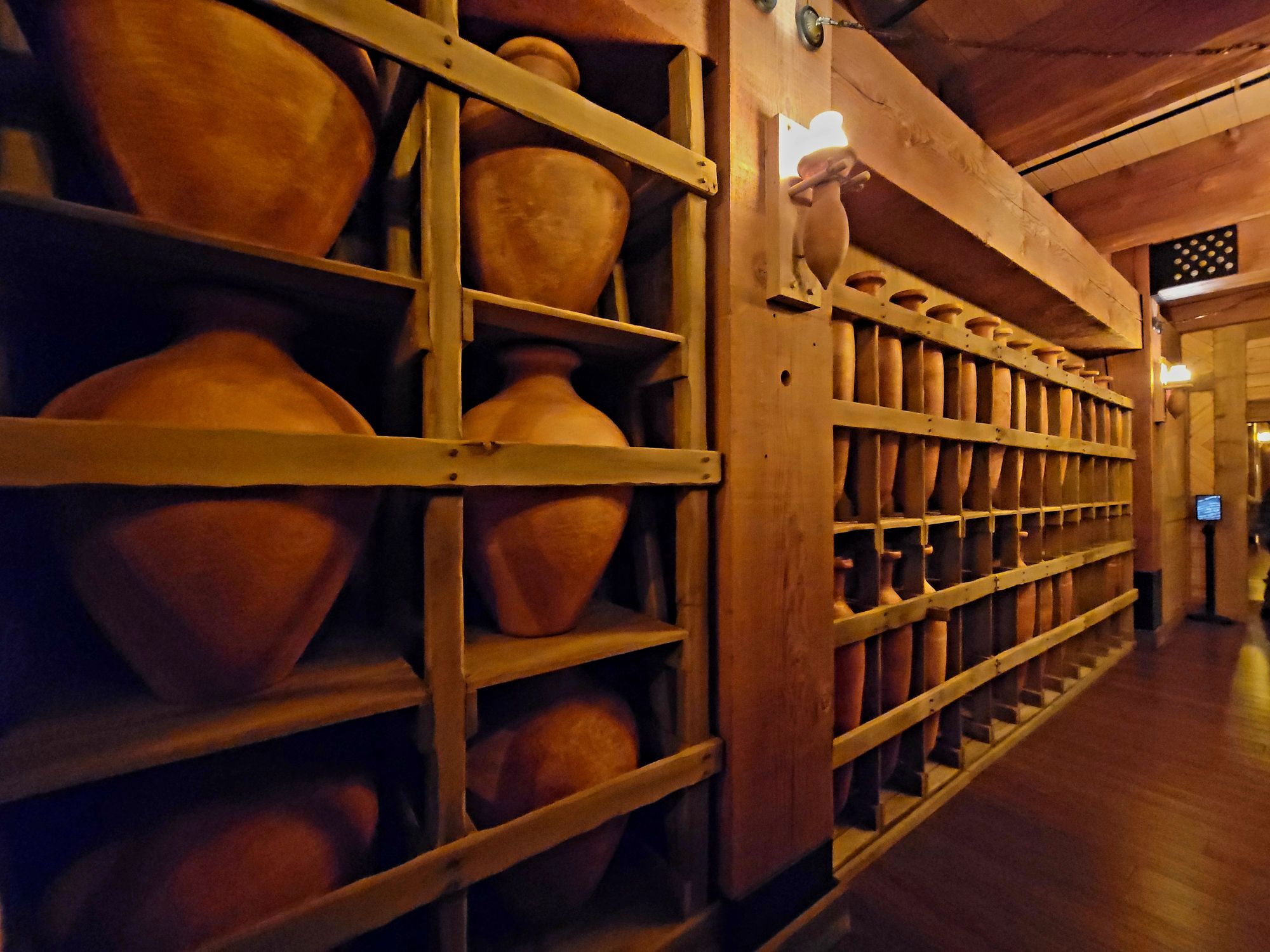 Interior view of a corridor lined with clay pots on wooden shelves, illuminated by warm lighting, resembling provisions on the Ark.