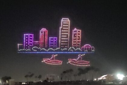 An aerial drone light show depicts a glowing cityscape with a two-boat formation below it, showcasing the spectacle of the St. Pete Fall Festival.