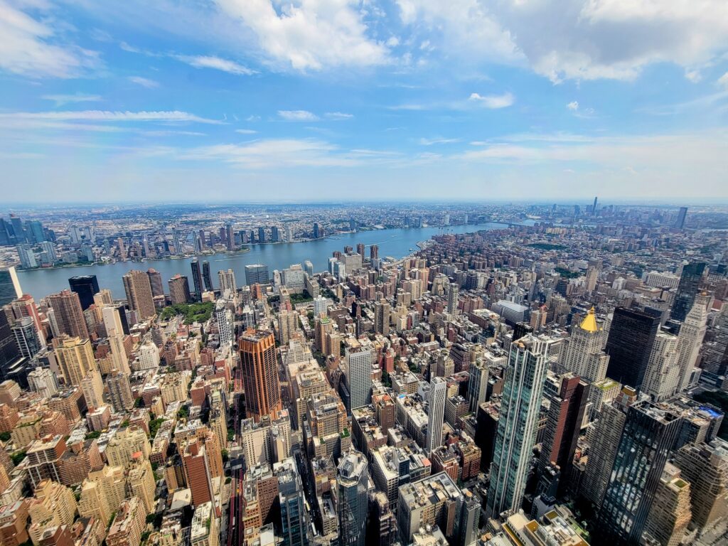 High-angle view of Midtown Manhattan with dense skyscrapers and Hudson River in the background—showcasing NYC’s architectural density and energy.