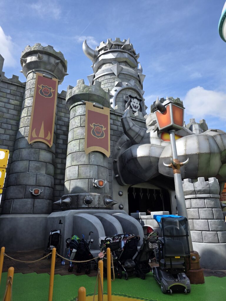 A large, castle-like structure inspired by a video game theme, featuring towers with spiked tops and banners. In the foreground, several strollers are lined up along a pathway.
