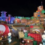 Nighttime view of Super Nintendo World at Universal's Epic Universe, featuring colorful buildings, Power-Up items, and the Toadstool Cafe, with visitors exploring the vibrant area.